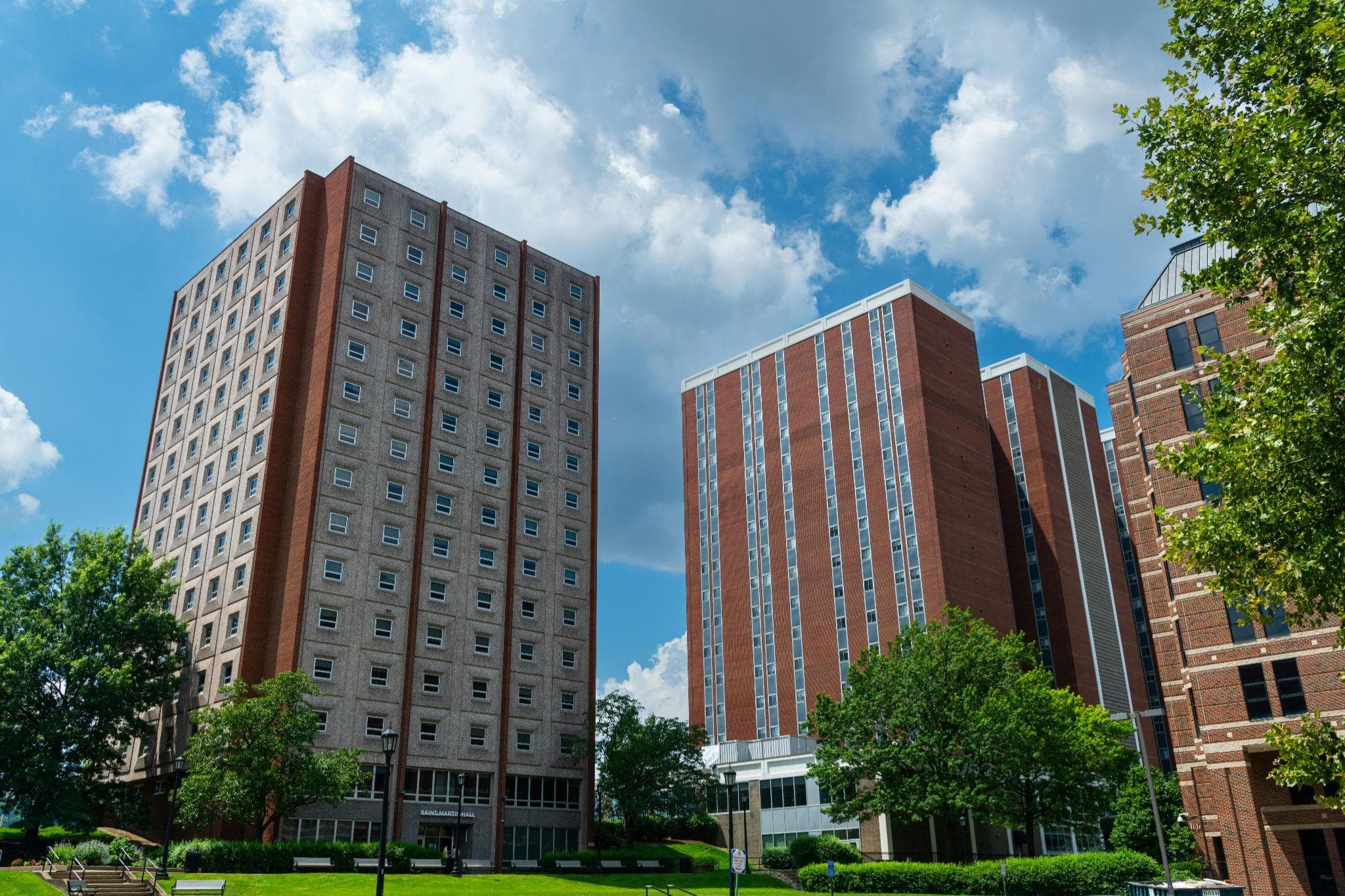 Low-angle view of brick university residence hall buildings under a partly cloudy sky.